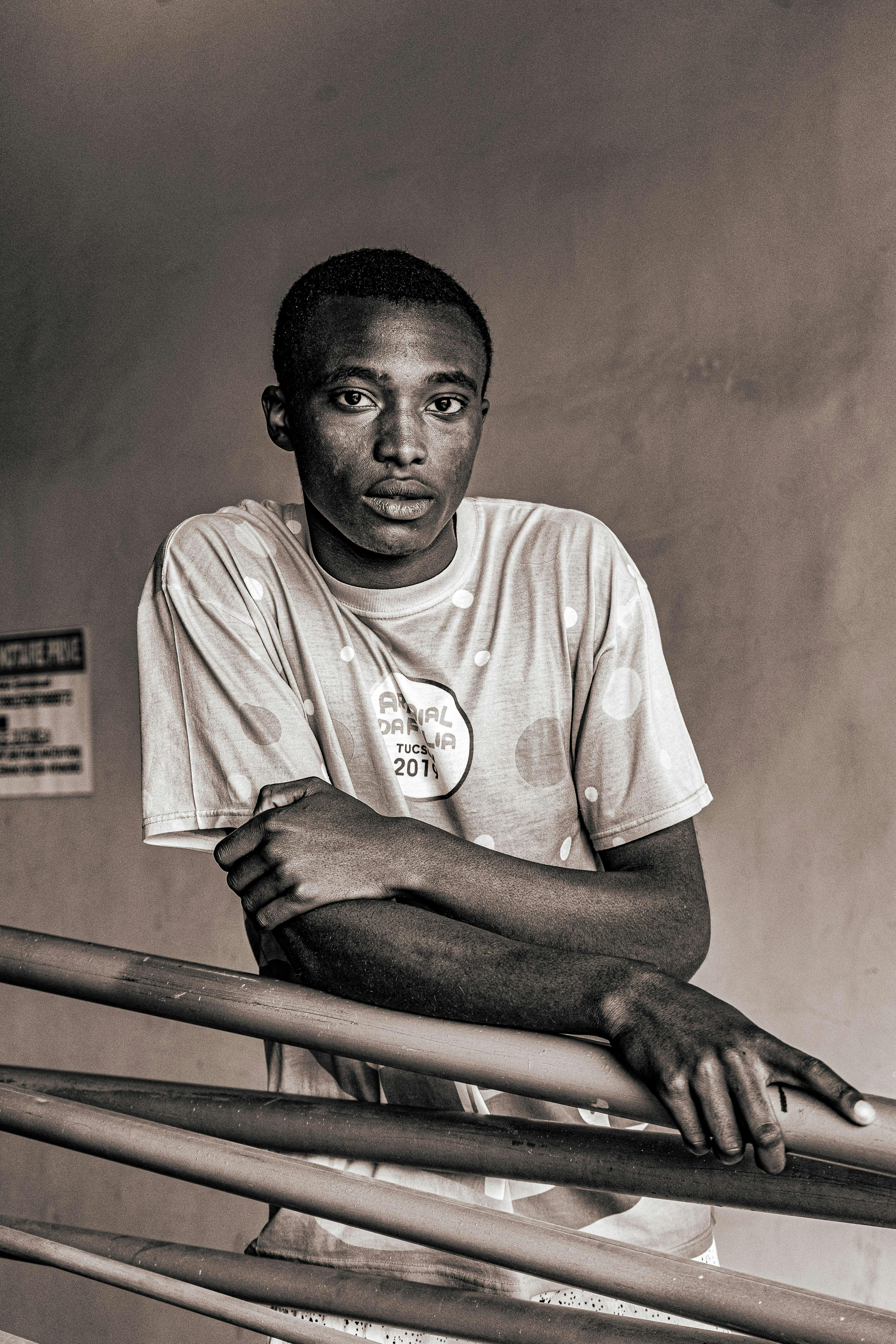 Artistic black and white portrait of a young man leaning on a railing, wearing a casual t-shirt.