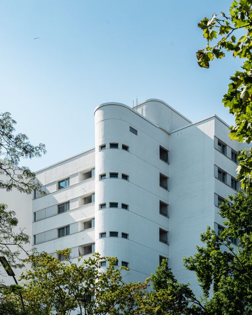 Contemporary apartment building with unique design featuring white facade and green foliage, set against a clear blue sky.