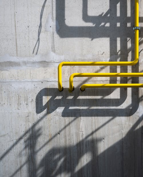 A yellow pipe is on the wall next to a concrete wall