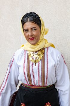 Woman wearing a traditional folklore costume with headscarf and necklace, smiling against a plain background. — photo by Boris Hamer