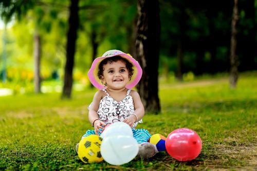 Free A cheerful young girl playing in the park with balloons and balls, exuding joy. Stock Photo