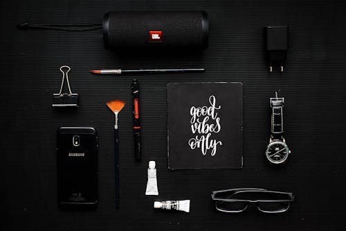 Free 智能手機在黑色紡織品上的活頁夾，揚聲器和眼鏡旁邊的特寫攝影 Stock Photo