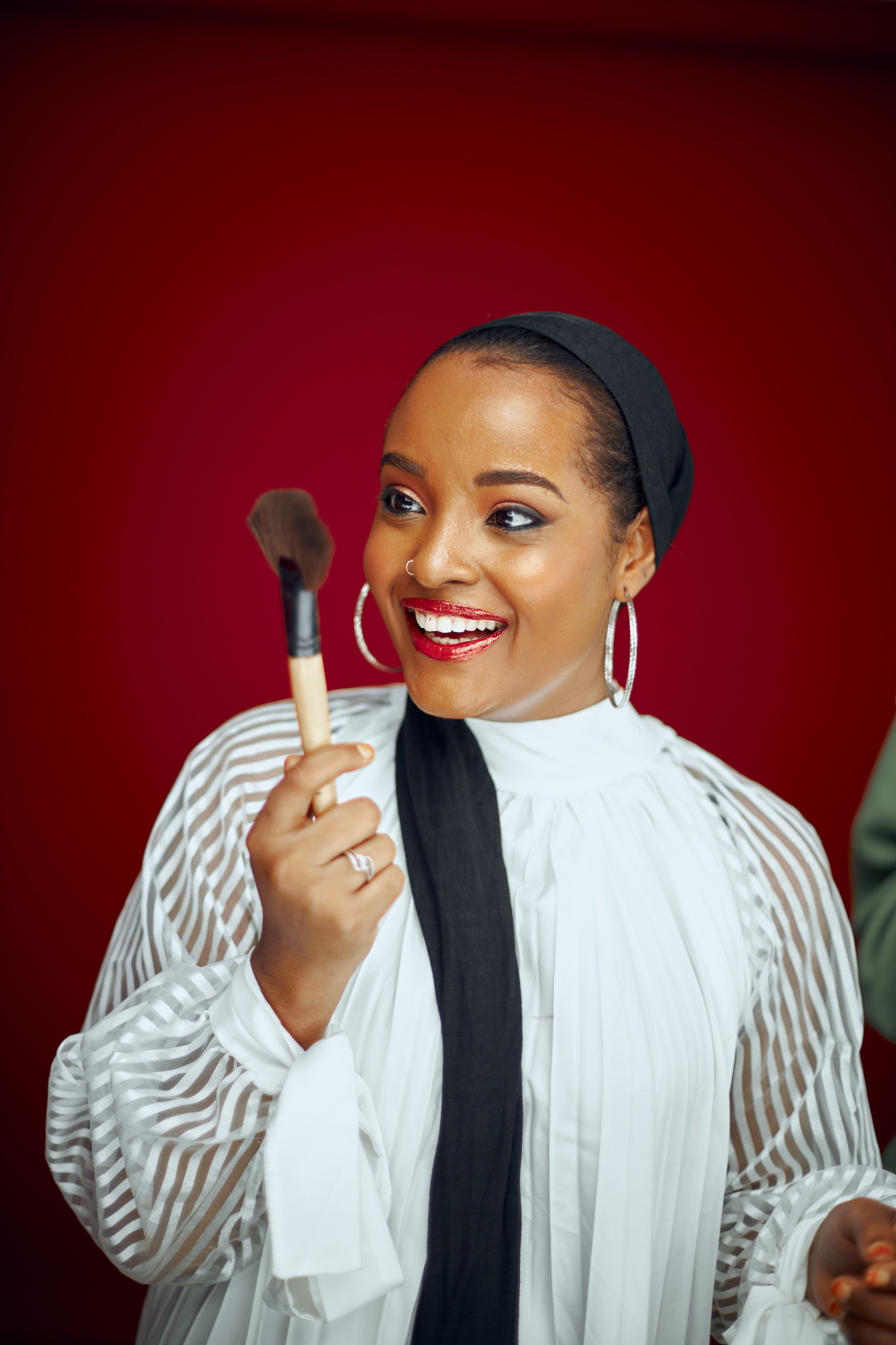 Vibrant studio portrait of a young woman cheerfully holding a makeup brush.