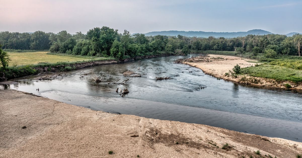 A serene river flows through a lush green landscape in Kellogg, Minnesota during summer.