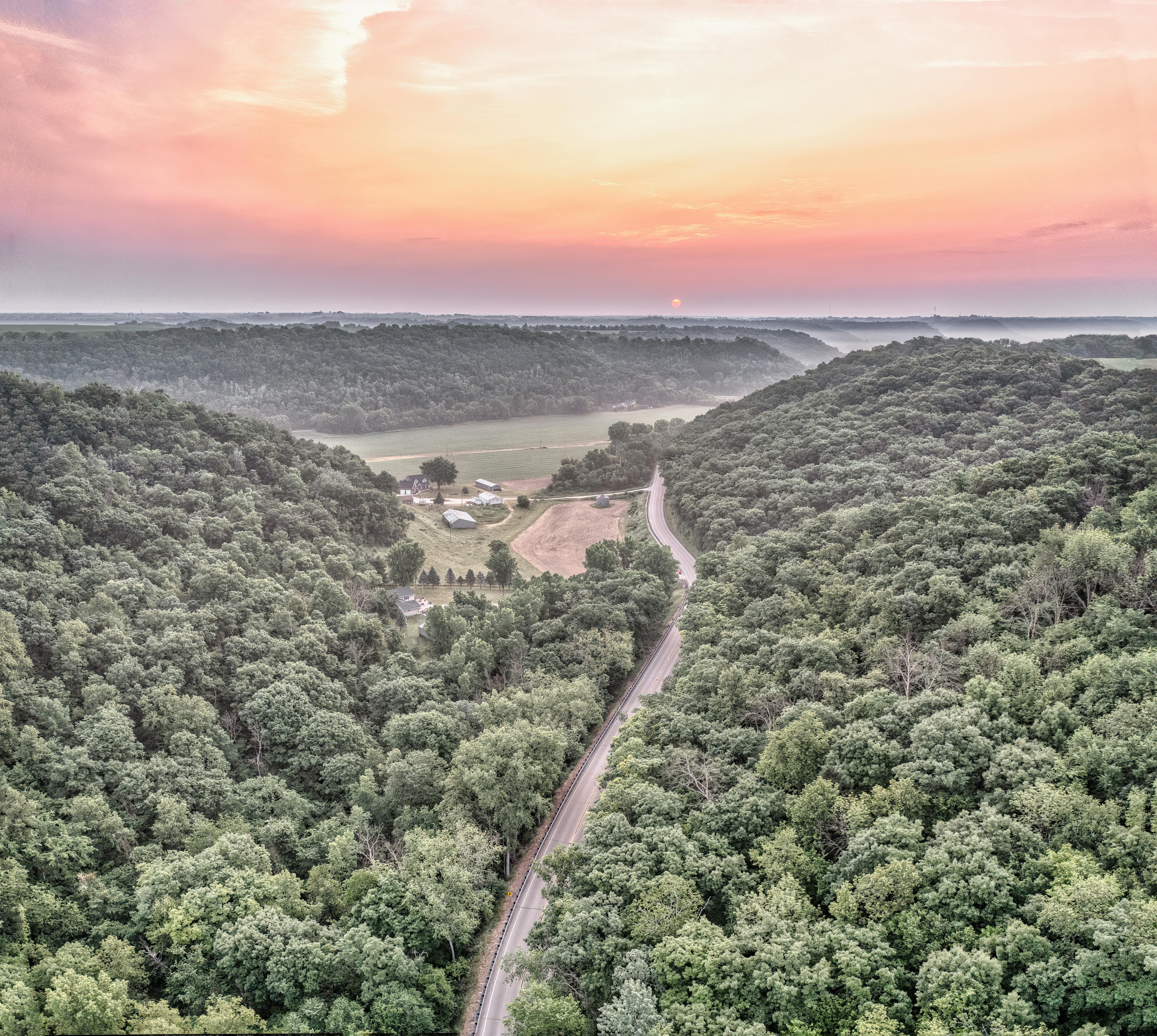 Stunning aerial shot of a winding road through a lush forest at sunset in West Albany, MN.