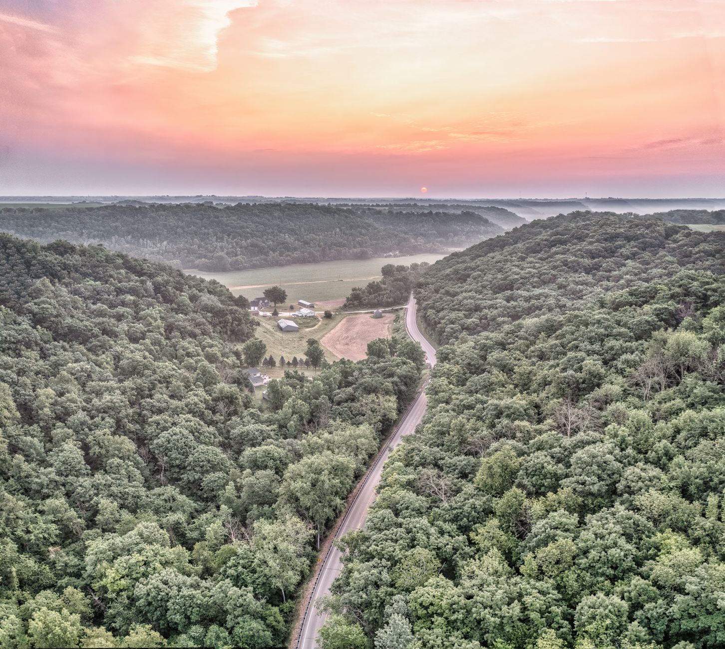Stunning aerial shot of a winding road through a lush forest at sunset in West Albany, MN.