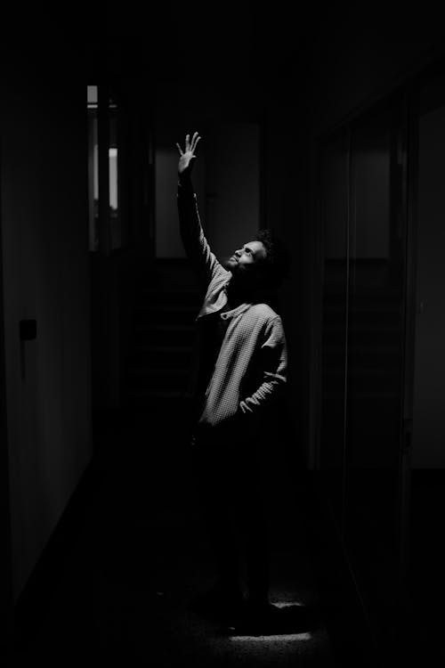 Man Looking Up with Raised Hands in Dark Corridor