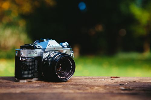 Free Close-up of a classic vintage analog camera on a wooden table outdoors, with a blurred green background. Stock Photo