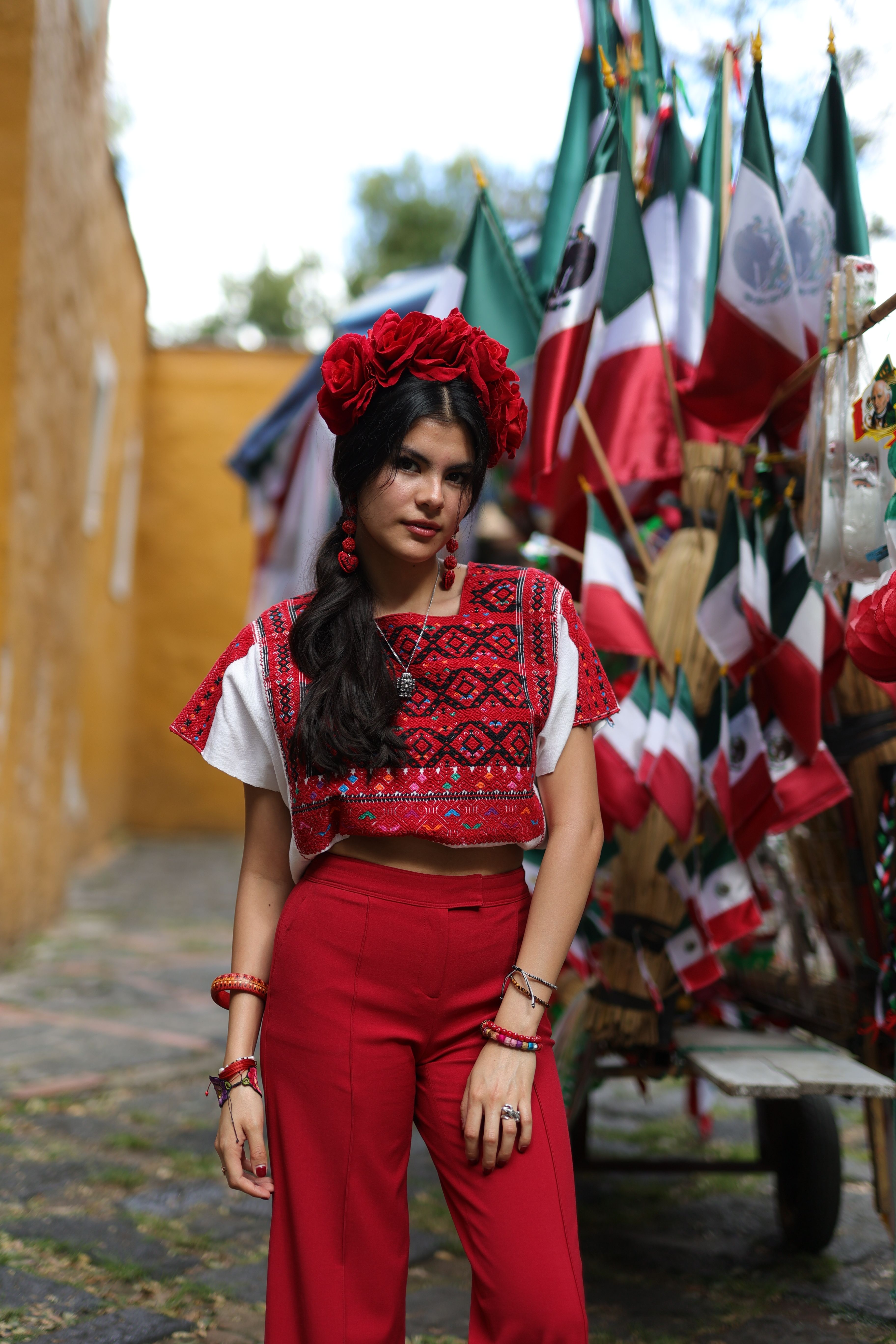 A young woman in vibrant traditional Mexican attire stands amidst a festive parade with flags.