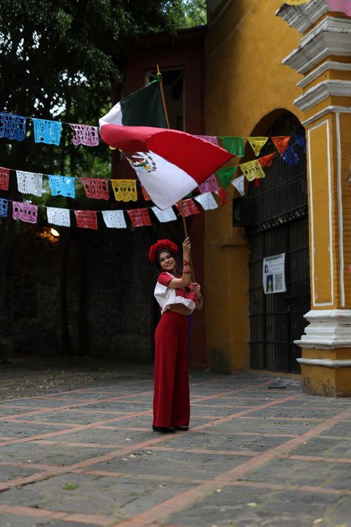 Free Adult woman in traditional Mexican attire waving flag in festive outdoor setting. Stock Photo