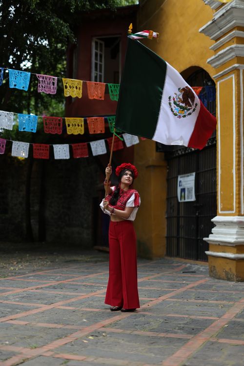 Free Woman in traditional attire holding a Mexican flag during a cultural festival outdoors. Stock Photo
