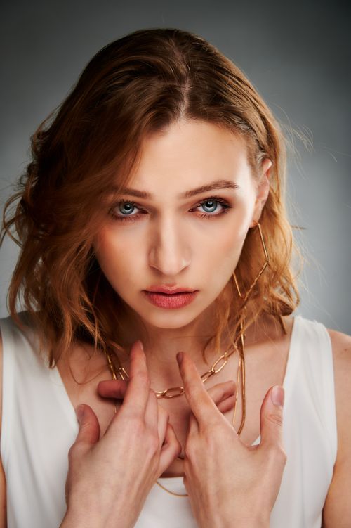 Free Close-up portrait of a young woman with blue eyes, wearing gold jewelry, in a studio setting. Stock Photo