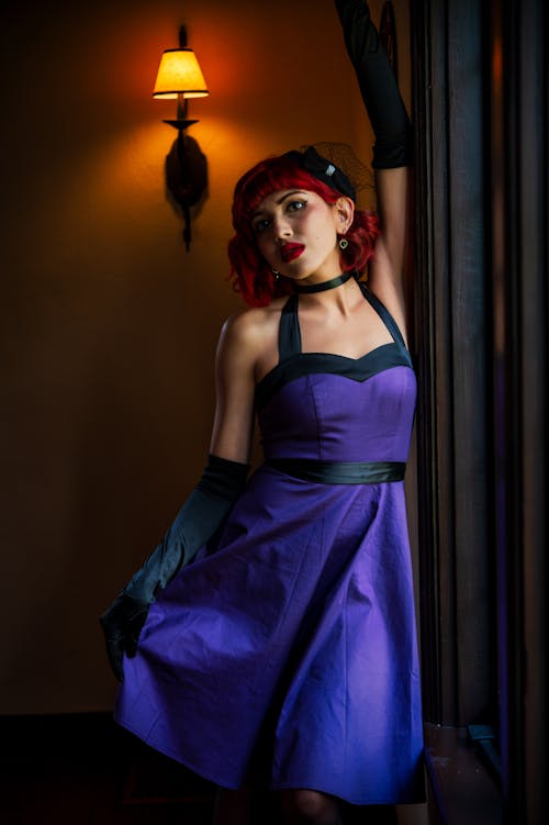 Young Woman in a Purple Dress and Gloves Posing in a Dark Room