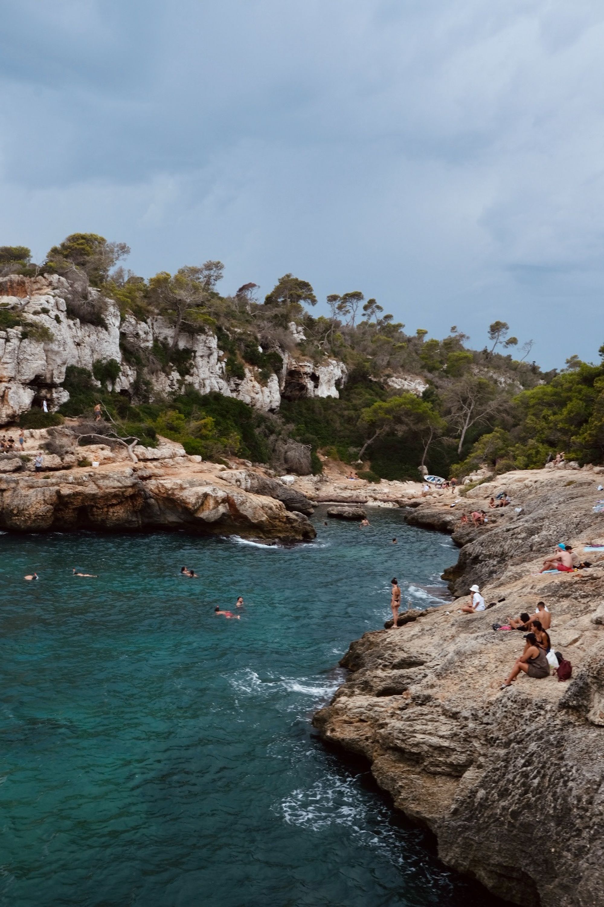 Tourists enjoy the rocky seashore at La Cala del Moral, Spain, surrounded by turquoise waters.