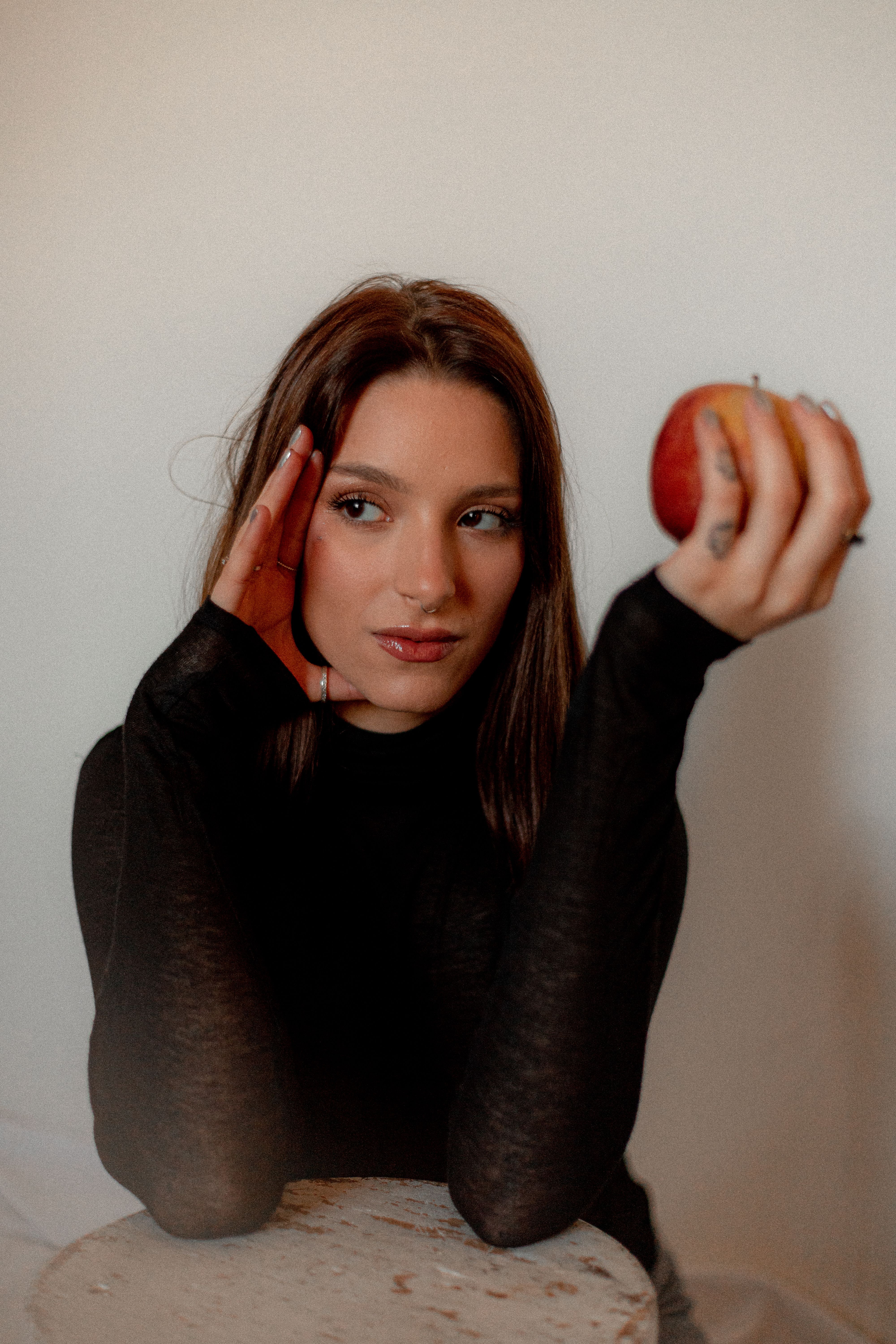 Young woman in black top holding an apple indoors. Casual portrait with soft lighting.