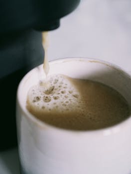 Close-up of hot coffee being poured into a ceramic cup with frothy bubbles.