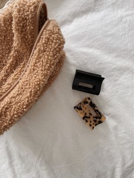 Beige zippered bag and hair clips on a white bed. Simple and cozy design.