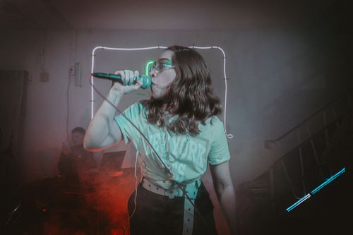 Free Woman singing into microphone in neon-lit indoor setting, rocking retro style. Stock Photo