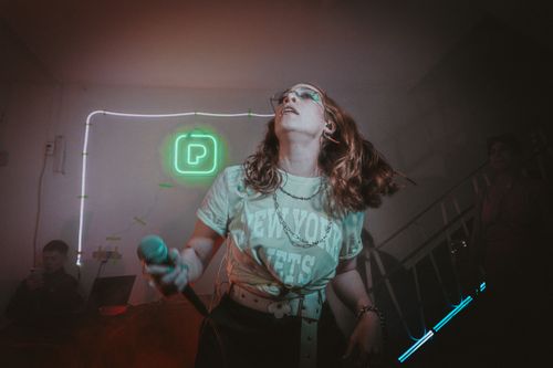 Free Singer performing with dynamic energy at a neon-lit indoor concert stage. Stock Photo