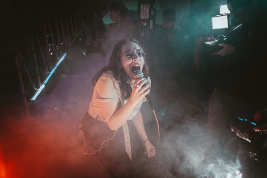 An energetic female singer passionately performs on stage amidst colorful lights and smoke.