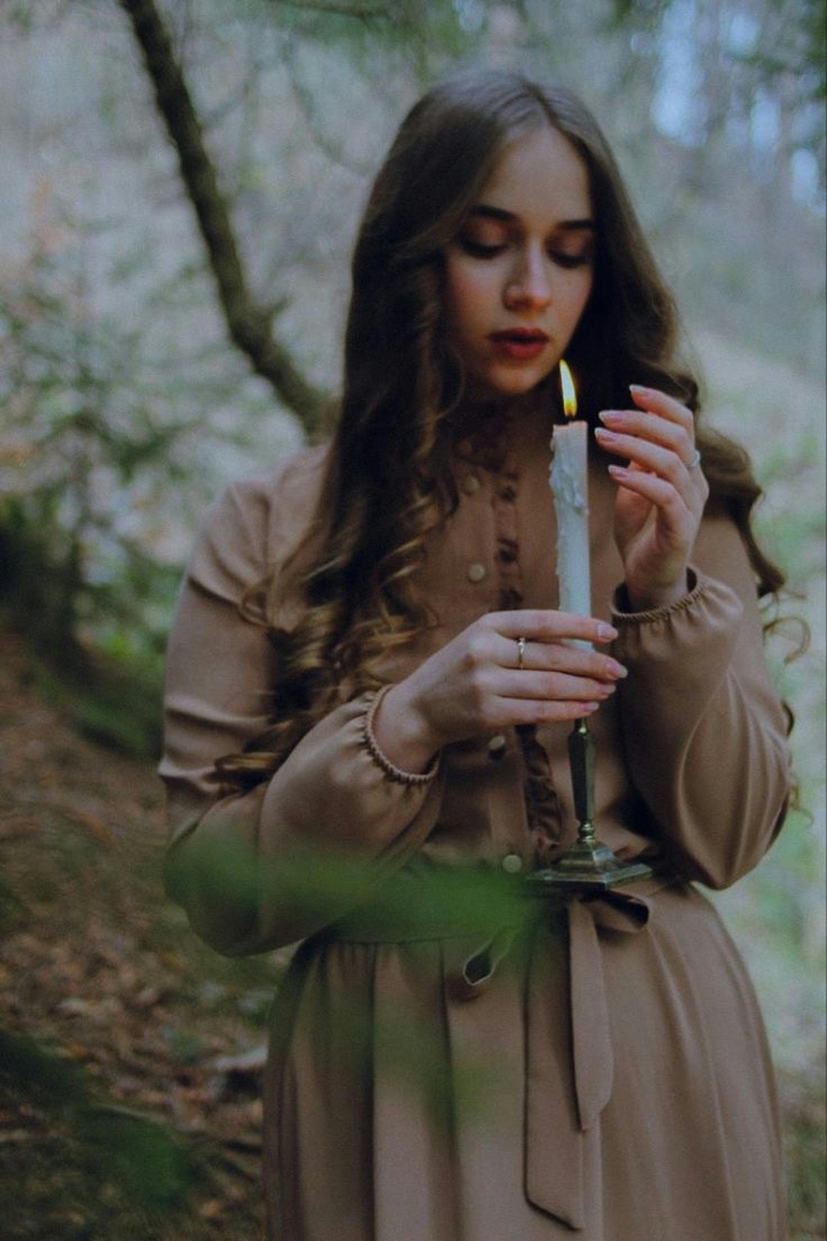 Young woman holding a candle in a serene forest, evoking a mystical and contemplative mood.