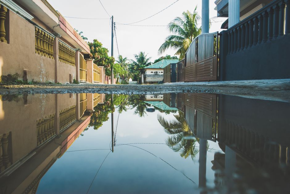 Mediterranean street with palm trees and low-rise houses reflected in a large rain puddle after a storm.