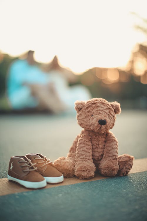 Brown Bear Plush Toy Beside Pair of Toddler's Brown-and-white Shoes on Ground in Selective Focus Photography