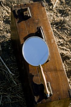 A rustic wooden box outdoors with a vintage handheld mirror reflecting sunlight.