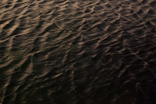 Free Gentle ripples on a water surface reflecting soft sunset light, creating a serene and textured pattern. Stock Photo
