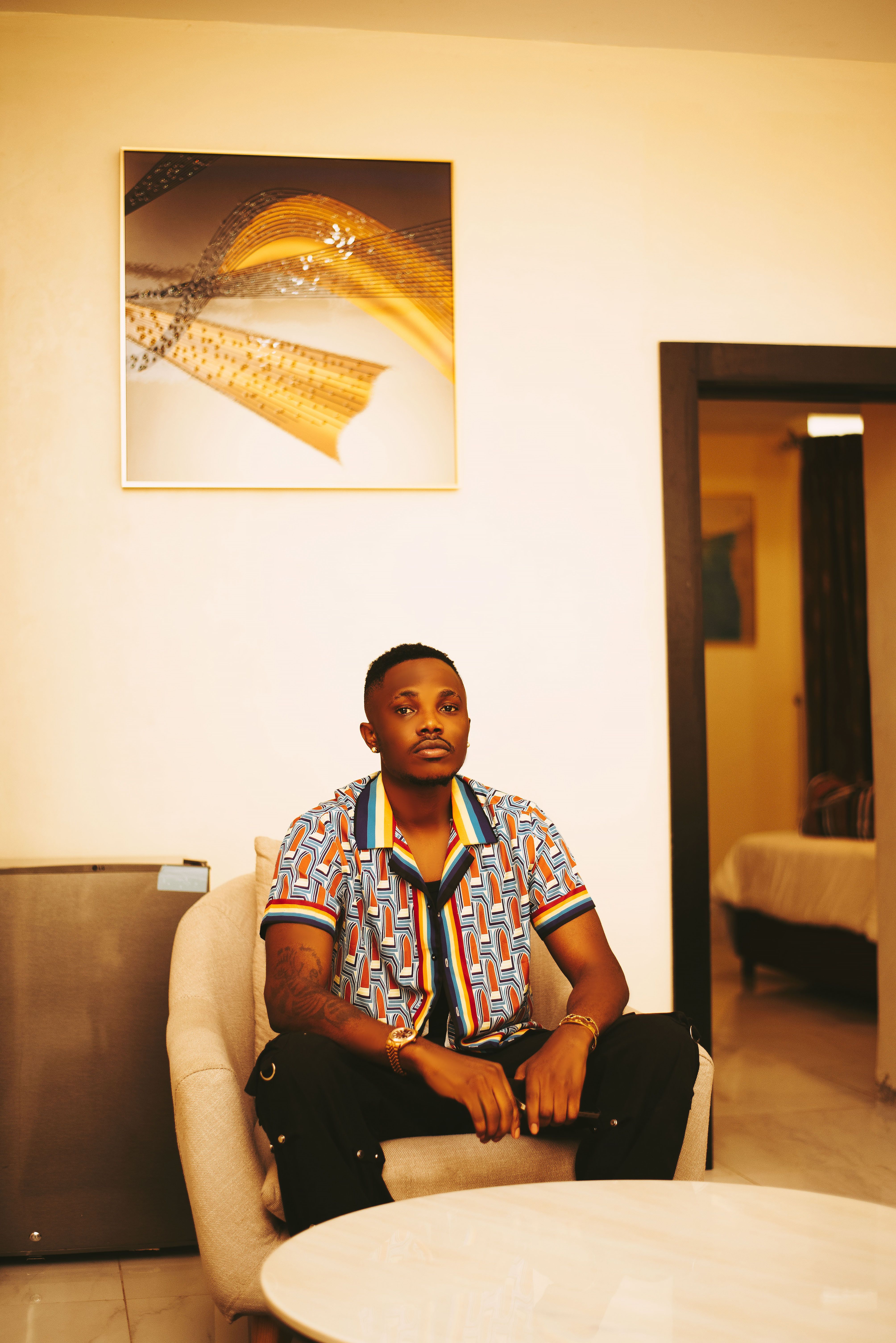 A stylish man sits in an armchair in a modern living room with contemporary art on the wall.