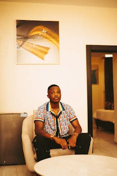 A stylish man sits in an armchair in a modern living room with contemporary art on the wall.