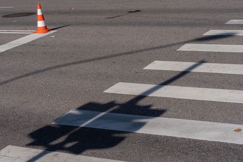 Free Street scene with a traffic cone, crosswalk, and shadows, capturing urban infrastructure. Stock Photo
