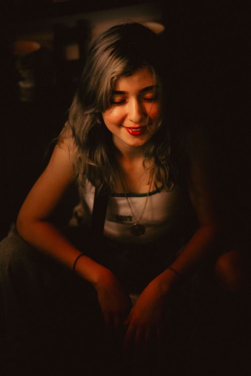 Free A warm and moody portrait of a smiling woman with long brown hair, sitting indoors. Stock Photo