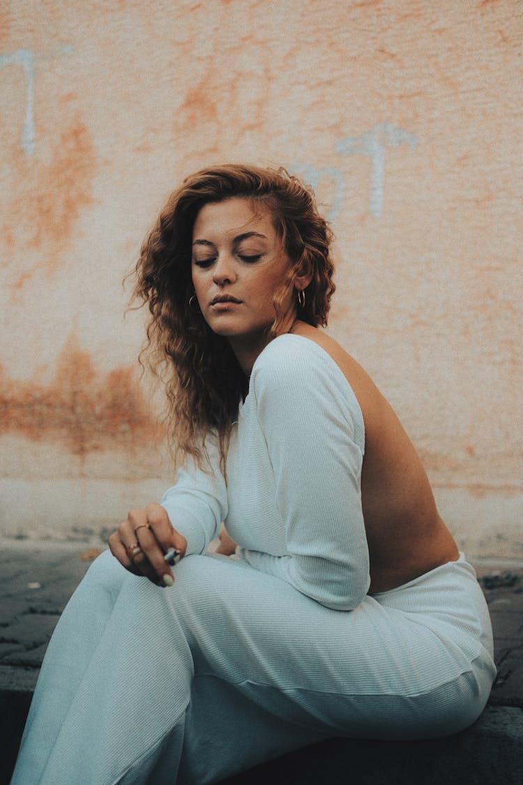 Woman Wearing Backless Suit Sitting On Ground Smoking Cigarette