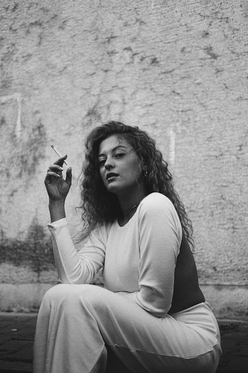 Young Woman Smoking a Cigarette Sitting on the Sidewalk