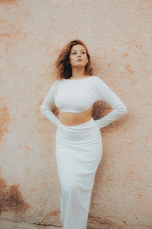 Model in a White Crop Top with Long Sleeves and a Maxi Skirt Against the Wall