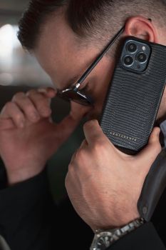Man holding a luxury leather phone case, dressed stylishly with sunglasses.