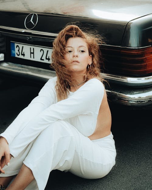 Woman in White Top Sitting on Asphalt Next to Mercedes Car