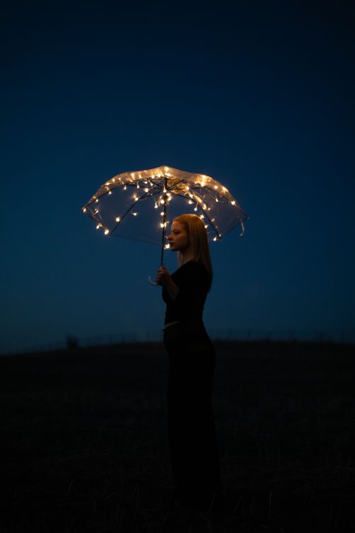 Free Atmospheric portrait of a woman standing outdoors with a lit umbrella against a dark night sky. Stock Photo