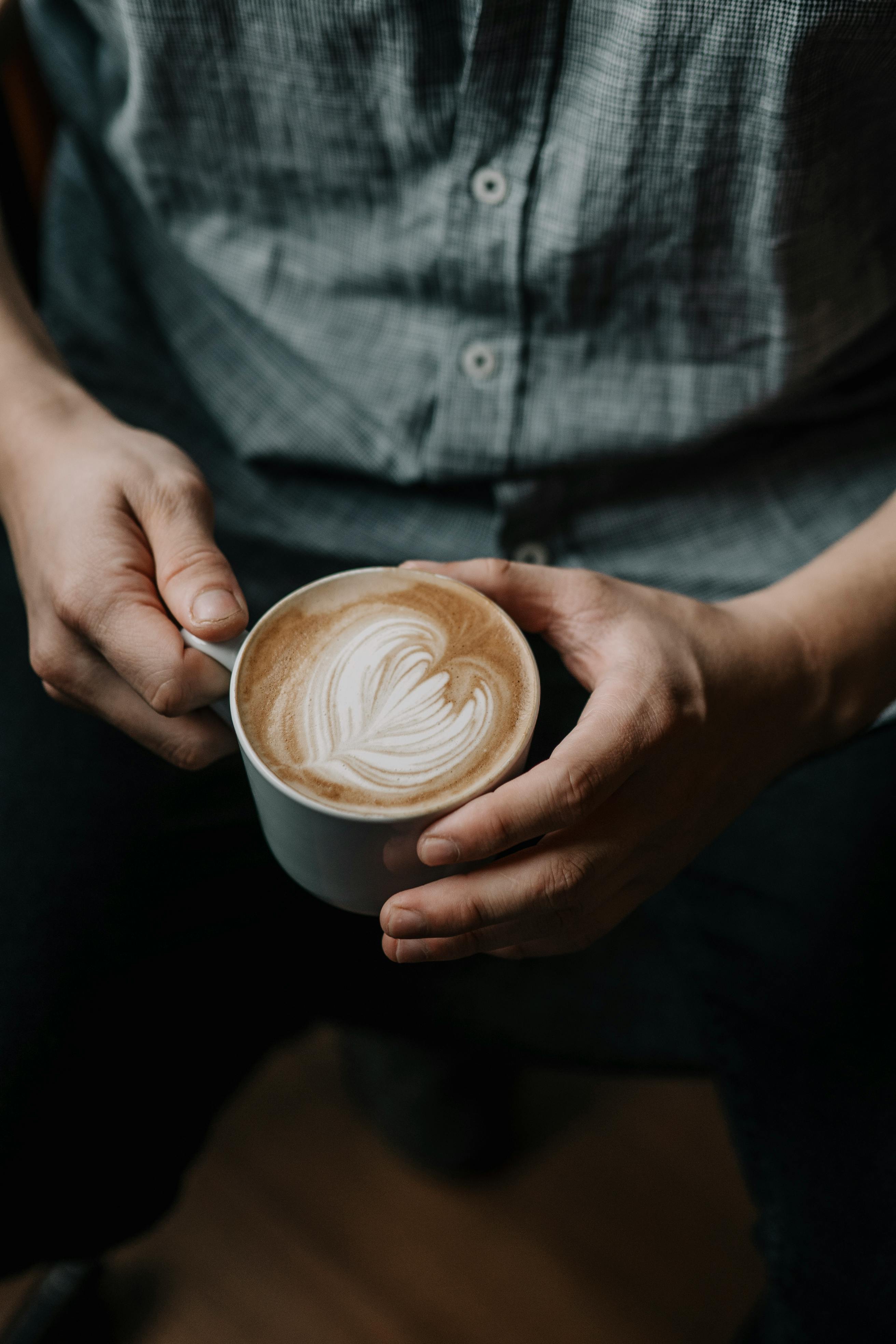 Close-up of hands holding a coffee cup featuring beautiful latte art.