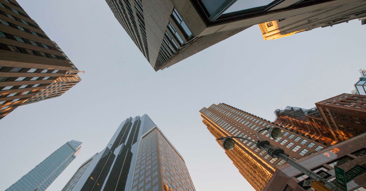 Dramatic upward view of modern skyscrapers creating an urban canyon against a clear sky.
