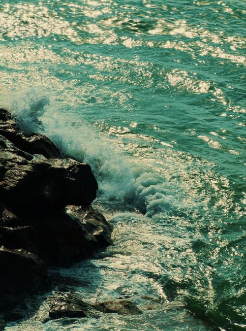 Free Vibrant waves crash against rocky shore, reflecting sunlight on a sunny day. Stock Photo