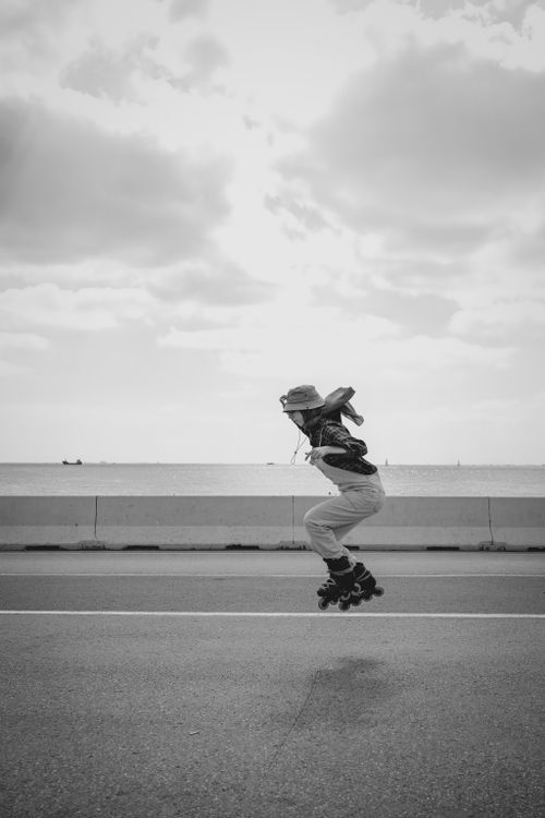 Free A young woman roller skating and jumping along a coastal road, evoking a sense of freedom. Stock Photo