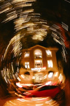 Blurred cityscape with swirling lights and illuminated house at night, creating an abstract effect.