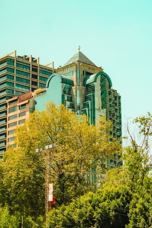 Free Glass-fronted skyscraper amidst green trees in Mexico City, showcasing urban architecture and nature. Stock Photo