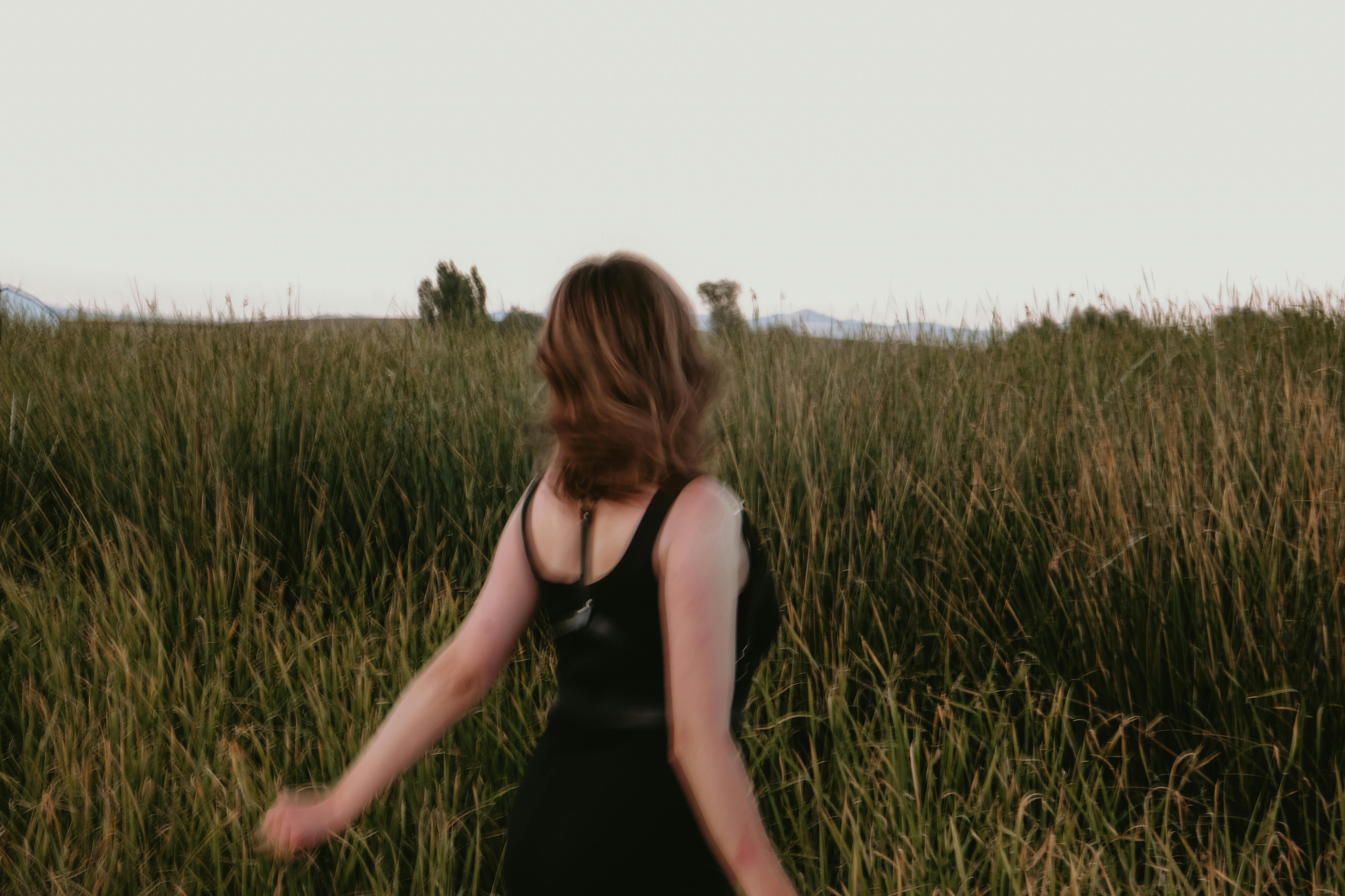 A woman in a black dress walking through a lush green field at twilight, embracing nature's tranquility.