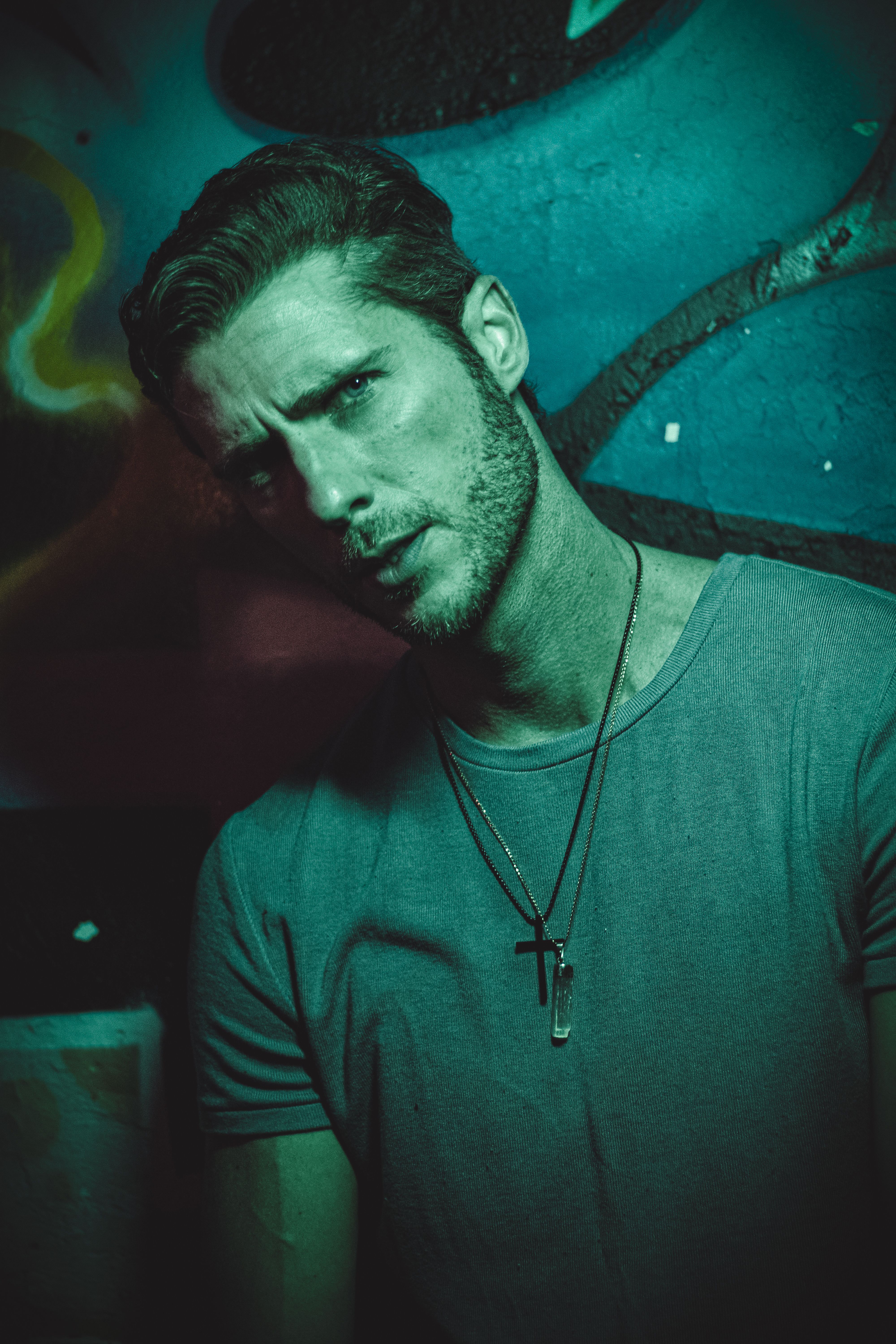 Stylish man with a beard posing indoors with vibrant lighting and graffiti background.