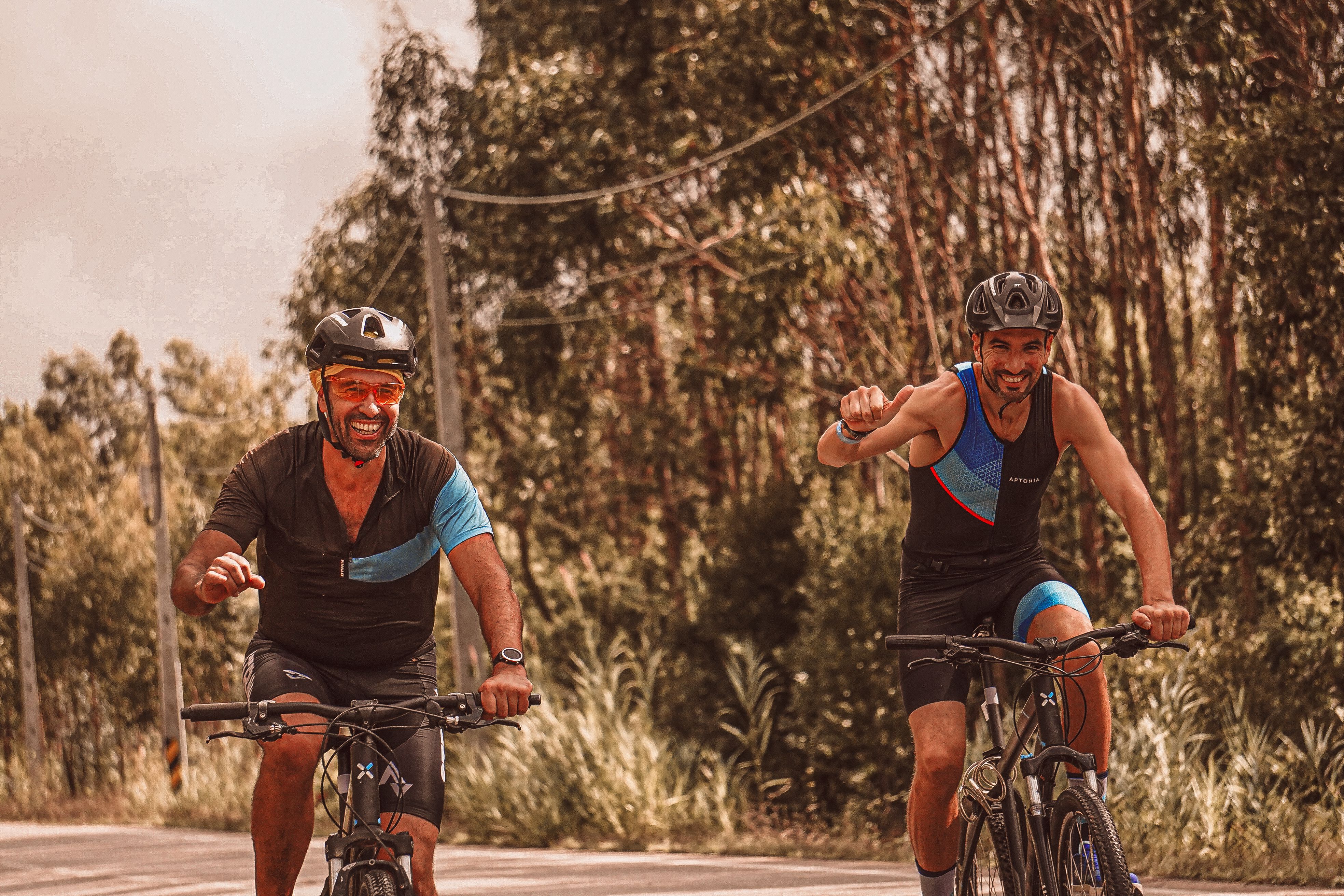 Two men cycling on a road during summer, smiling and enjoying the ride.
