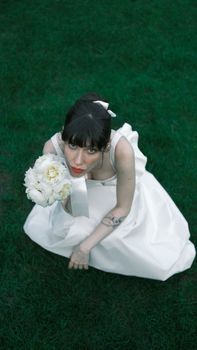 Bride in wedding dress holding a white bouquet, posing on lush green grass.
