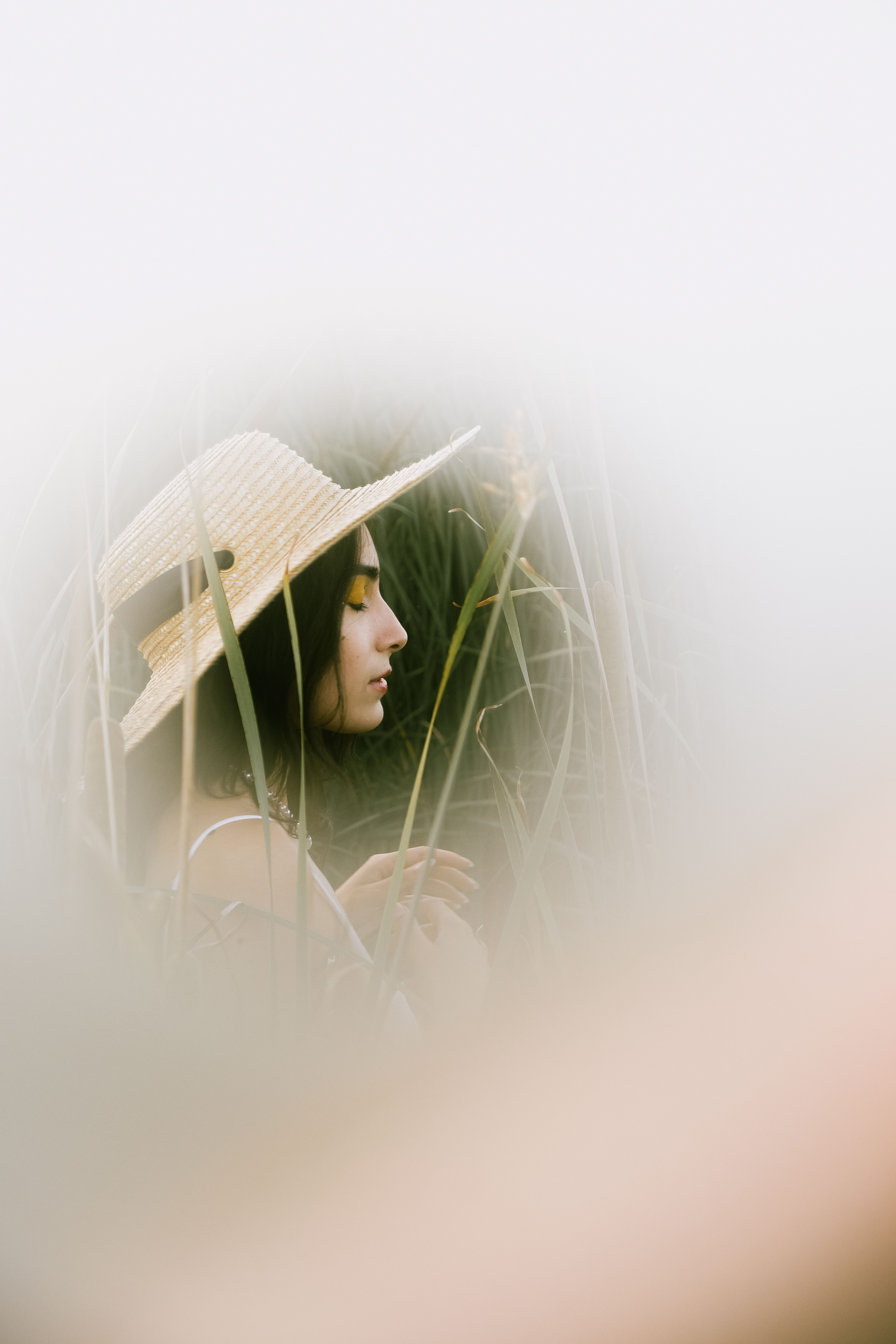 Artistic portrait of a woman in a straw hat surrounded by tall grass during summer.